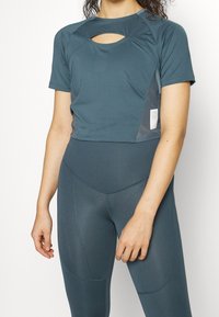 Tyrkysový sportovní crop top s kulatým výřezem, texturovaná látka a krátké rukávy, spárovaný s odpovídajícími legínami s vysokým pasem a bočními švy.