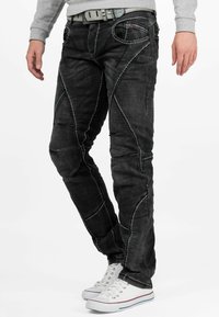 Zwarte denim jeans met contrasterende witte stiksels, met een slim fit en unieke paneelconstructie, gecombineerd met witte sneakers.