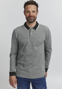 Siva dolgih rokavov polo majica z črnim ovratnikom in manšetami, ki ima gumbasto zapiranje in majhen prugast logotip na prsih.