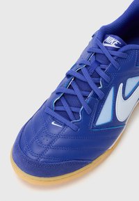 Blauer Sportschuh mit strukturiertem Synthetik-Obermaterial, Netzeinsätzen und gummierter Außensohle. Verfügt über einen weißen Swoosh und ein detailliertes Stichmuster.