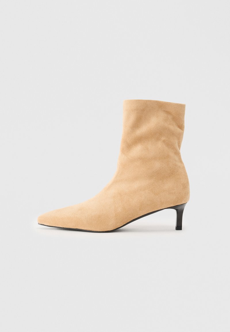 Beige semsket støvel med spiss tå og lav svart kitten-hæl på en enkel hvit bakgrunn.