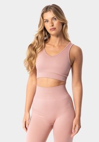 Sujetador deportivo rosa claro con un diseño de escote en V y banda acanalada, combinado con leggings de talle alto a juego. Textura suave, detalles mínimos.