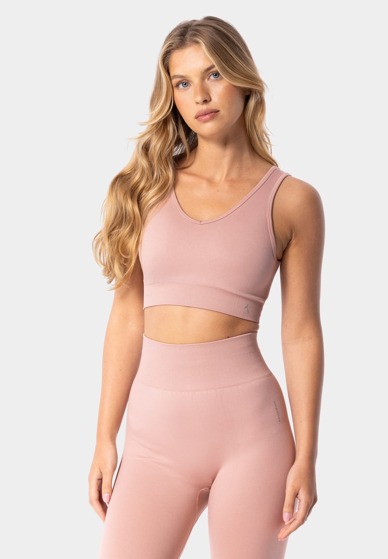Sujetador deportivo rosa claro con un diseño de escote en V y banda acanalada, combinado con leggings de talle alto a juego. Textura suave, detalles mínimos.