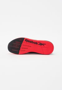 Reebok-sålen, overvejende rød med sorte sektioner, har strukturerede grebsmønstre og forhøjede bogstaver for bedre traektion.