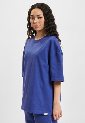 Overdimensioneret blå bomulds T-shirt med korte ærmer og rund halsudskæring. Har et lille mærke nær kanten. Glat tekstur.