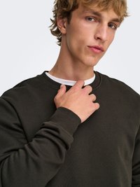 Mørkegrøn crewneck-sweatshirt lavet af blødt stof, med ribbede ærmegab og en tekstureret finish, samt en synlig hvid lagdelt krave.