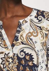 Blusa multicolore con motivo paisley in navy, oro e crema. Presenta un colletto a V e dettagli con bottoni al colletto.