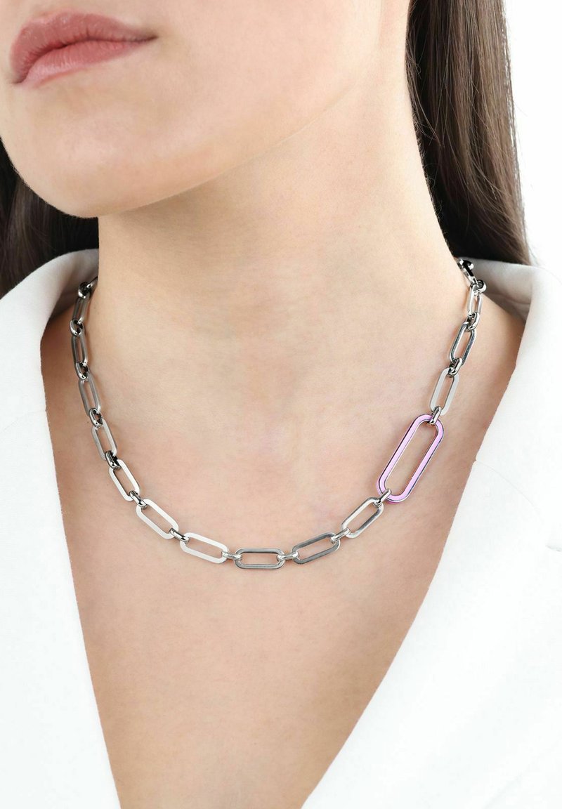 Collar de cadena de metal plateado con eslabones alargados, que presenta un eslabón de acento morado. Se lleva cerca del cuello, resaltando un diseño moderno.