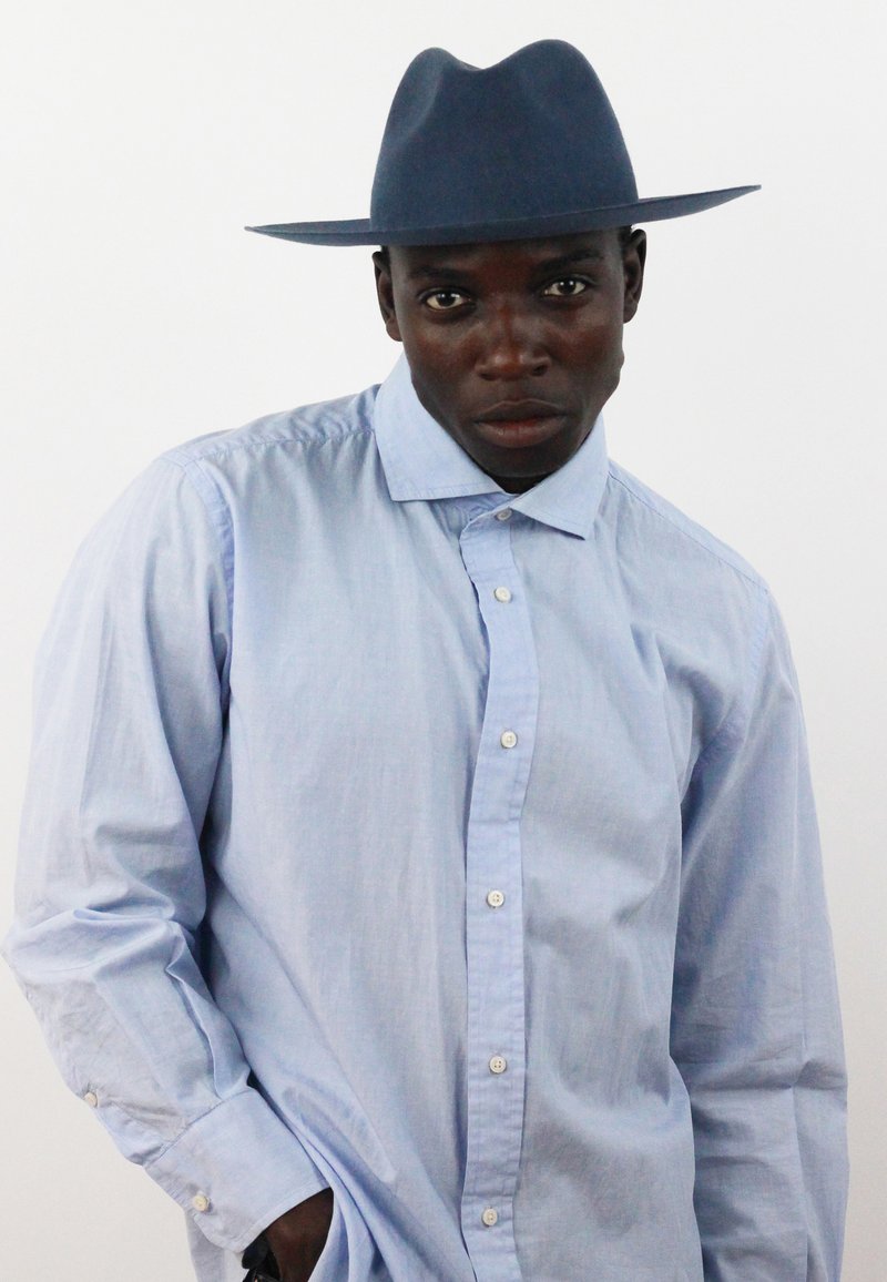 Hemd in Hellblau mit langen Ärmeln und klassischem Kragen, kombiniert mit einem dunkelblauen Hut mit breiter Krempe.