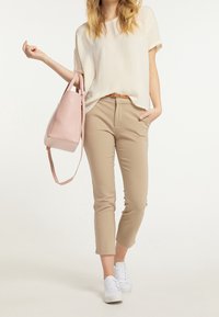 Pantalon beige fuselé, haut à manches courtes crème clair, sac à main rose avec bandoulière, baskets blanches ; ensemble de tenue décontractée et moderne.