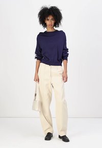 Felpa blu navy con scollatura ampia, pantaloni cream a gamba larga, scarpe nere e una piccola borsa cream. Tessuto testurizzato con una vestibilità rilassata.