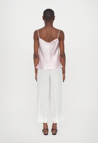 Rosa satengcamisole med tynne stropper, parret med hvite vide linbukser med oppbrett i kanten. Enkelt, glatt tekstur og lett design.
