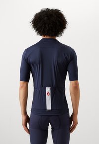 Maillot de cyclisme bleu marine à manches courtes, à coupe ajustée, avec une bande d'accent blanche à l'arrière et un écusson logo près de l'ourlet. Texture lisse.