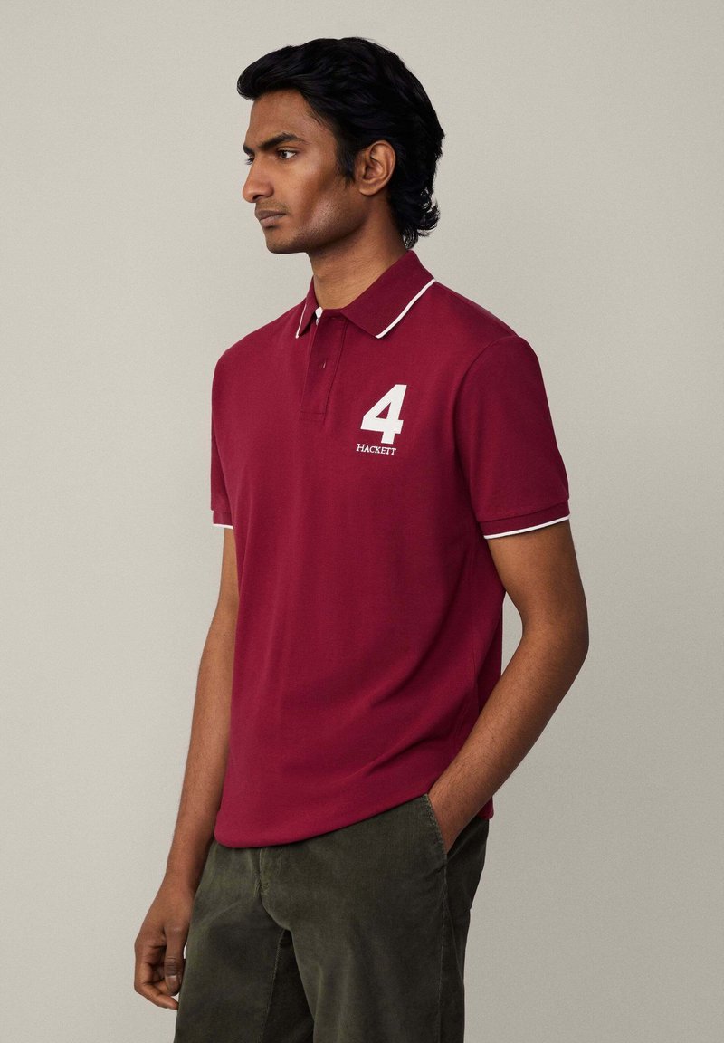 Bordový polo tričko s bielym lemovaním a golierom. Na prednej strane je biele číslo "4" a názov značky "HACKETT". Krátke rukávy.