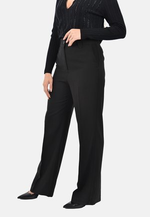 Pantaloni neri a gamba larga con una texture liscia, dotati di tasche laterali e chiusura con bottone, abbinati a un top a maniche lunghe a coste.