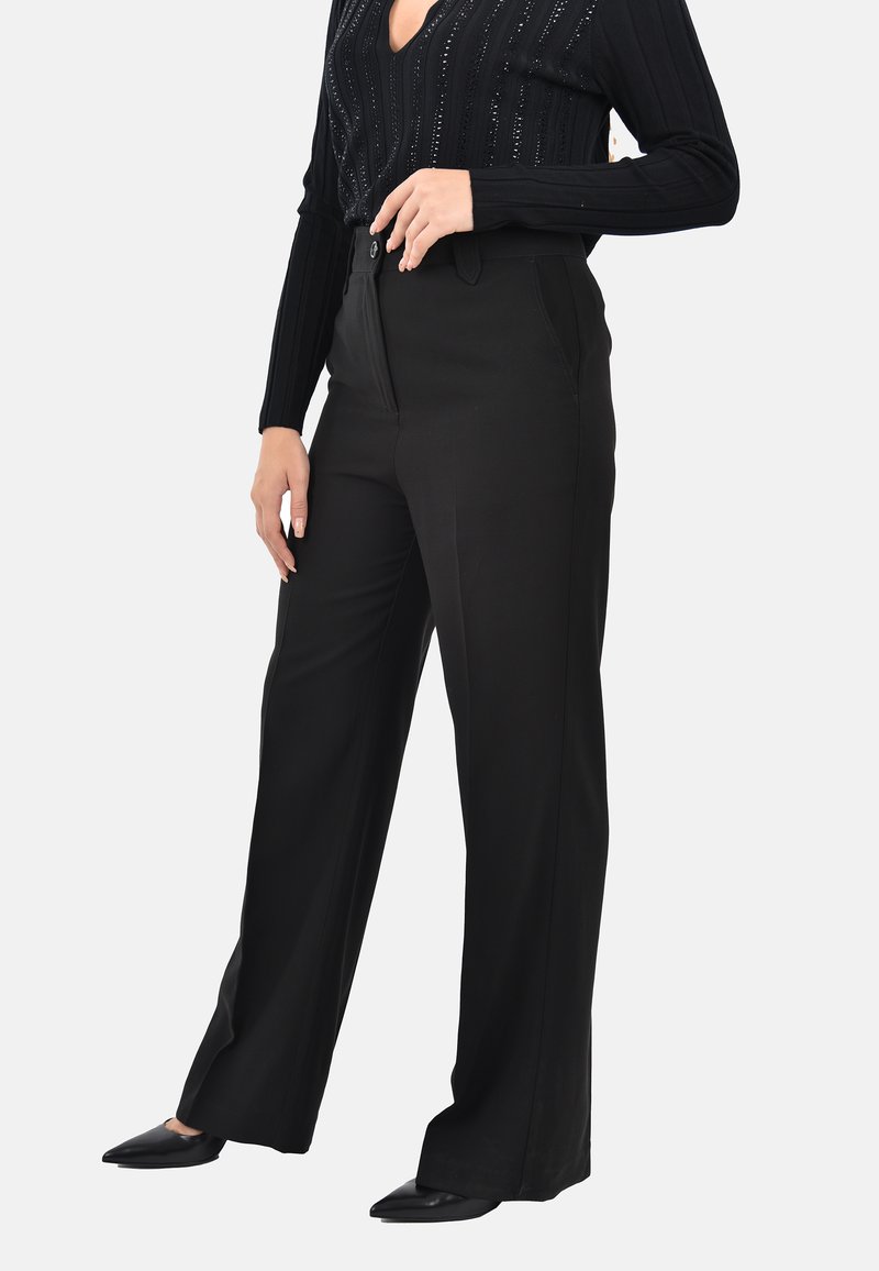 Pantaloni neri a gamba larga con una texture liscia, dotati di tasche laterali e chiusura con bottone, abbinati a un top a maniche lunghe a coste.