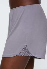 Szare bawełniane szorty z falbanką na dole, zdobione koronkowym detalem. Tkanina jest gładka, z luźnym krojem i elastycznym paskiem w talii.