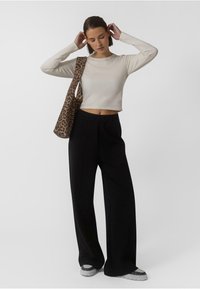 Crop top crème à manches longues associé à un pantalon large noir. Accessoirisé avec un sac à épaule à imprimé léopard. Look décontracté et fit relax.