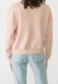 Helles rosa Sweatshirt mit Rundhalsausschnitt, überschnittenen Schultern und geripptem Saum. Kombiniert mit hellblauen, hochgeschnittenen Jeans. Einfaches, lässiges Design.