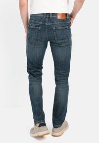 Blaue Denim-Jeans mit schlankem Schnitt, fünf Taschen und Lederpatch am hinteren Bund. Kombiniere sie mit beigen Sneakers.