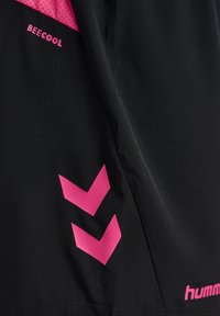 Svart atletisk topp av slät tyg, med rosa meshinlägg och logotyper. Utmärkande rosa chevronmönster på sidan och varumärkesnamnet.