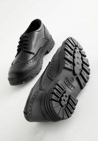 Chaussures noires en cuir avec un design à lacets, des détails en brogue et des semelles en caoutchouc épais dotées d'un profilé pour une meilleure adhérence.