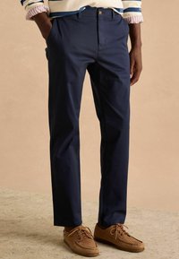 Donkerblauwe chino's met een recht model, voorzien van zijzakken en een subtiele glans, gecombineerd met bruine veterschoenen.