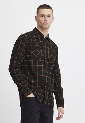 Sort ternet skjorte med orange rutenet, med to brystlommer og knaplukning. Stoffet fremstår blødt og tekstureret.