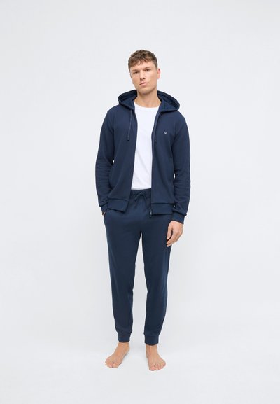 Mornarica zip-hoodie s vezicom, uparena s odgovarajućim hlačama. Oboje izrađeno od mekog materijala, s rebrastim manžetama i pojasom.