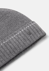 Bonnet gris en tricot avec revers côtelé, détail blanc cousu et petit emblème noir en métal en forme de "B" sur le revers, sur fond blanc.