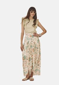 Top verde claro con volantes combinado con una falda larga de estampado floral en suave melocotón, con acentos en verde y marrón. Lleva consigo sandalias planas.