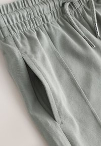Svetlošedé nohavice z texturovanej tkaniny s elastickým pásom, bočným vreckom a sťahovacou šnúrkou s kovovými koncami.
