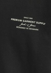 Tessuto nero con superficie liscia, con testo bianco: "Fornitura di Abbigliamento Premium" e "Progettato in Danimarca" in un font serif moderno.
