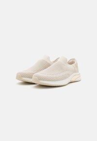 Baskets slip-on en maille beige clair avec surface texturée ; semelle blanche avec un accent doré subtil au talon ; design lisse et flexible.