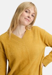 Musztardowożółty sweter z fakturą dzianiny z dekoltem w serek i długimi rękawami, o luźnym kroju i miękkim, puszystym materiale.
