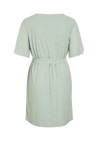 Ljusgrön klänning tillverkad av texturerad tyg, med korta ärmar, midja med bälte och ögla mönster över hela. Bakvy visas.