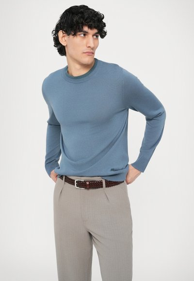 Jasnoniebieski sweter z fakturowanym wzorem i prążkowanym dekoltem, zestawiony z beżowymi, dopasowanymi spodniami i brązowym plecionym paskiem.