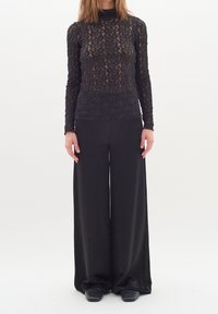 Haut en dentelle noire à manches longues avec un col haut, associé à un pantalon noir à jambes larges. Les deux pièces présentent une texture lisse et un design élégant.