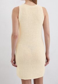 Abito lavorato a maglia giallo chiaro, senza maniche, con un motivo testurizzato, taglio dritto e orlo arrotondato all'altezza della coscia.