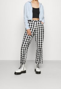 Felpa blu chiaro tagliata, top nero corto, pantaloni a quadri bianco e nero, e stivali bianchi con lacci e suola nera spessa.