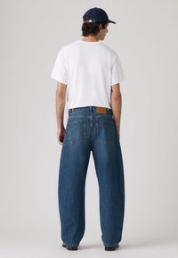 Ανοιχτό μπλε oversized τζιν παντελόνι με χαλαρή εφαρμογή και ίσια μπατζάκια, με δύο πίσω τσέπες και καφέ ετικέτα μάρκας στη μέση.