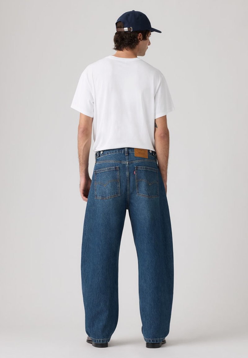 Pantalones vaqueros de mezclilla azul claro, de gran tamaño, con un ajuste holgado y piernas rectas, que cuentan con dos bolsillos traseros y una etiqueta de marca marrón en la cintura.