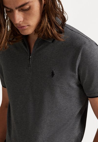 Polo gri închis cu guler cu jumătate de fermoar. Prezintă un logo subtil pe partea stângă a pieptului și un material texturat pentru un aspect modern.