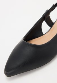 Μαύρο δερμάτινο παπούτσι slingback με μυτερή μύτη, χαμηλές πλαϊνές πλευρές και λεπτό τακούνι. Λείο υφή με μινιμαλιστικό σχέδιο.