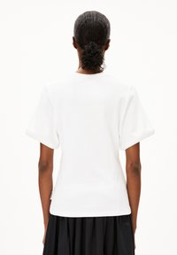 Weißes Kurzarm-T-Shirt mit lockerem Schnitt, gerippter Textur und rundem Halsausschnitt, kombiniert mit einem fließenden schwarzen Rock.