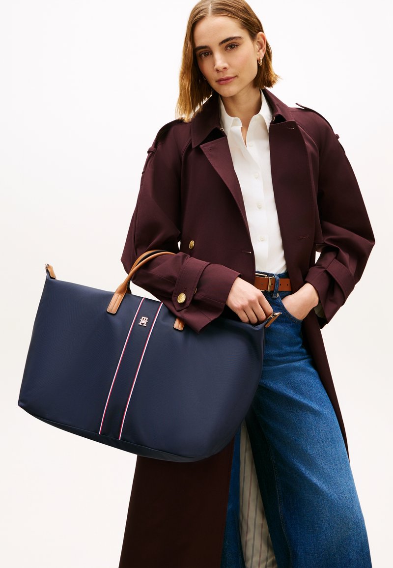 Τσάντα ώμου σε ναυτικό μπλε με χειρολαβές από ταμπά δέρμα, με κεντρικό λογότυπο και διπλές ροζ ρίγες. Υφασμάτινη υφή, ευρύχωρος σχεδιασμός και στρογγυλεμένες άκρες.