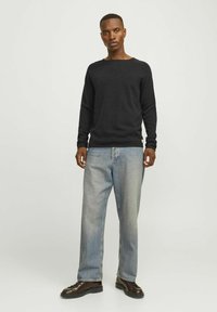 Maglione a maniche lunghe nero in maglia con scollo a girocollo, abbinato a jeans larghi blu chiaro e scarpe scure con lacci. Design semplice; nessun motivo visibile.