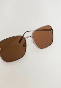 Sunglasögon med bruna tonade linser, metallram och strukturerade silverdetaljer. Fyrkantig form med justerbara näskuddar och smala templer.