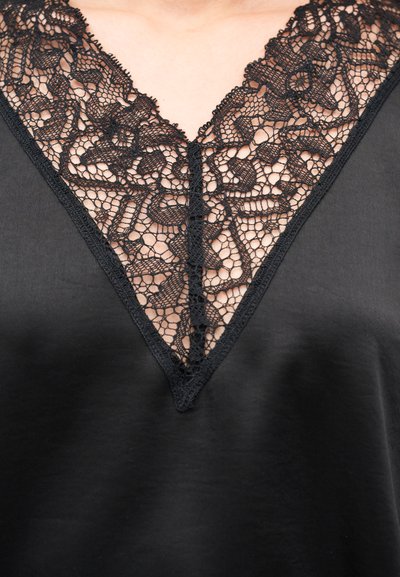 Μαύρο υφασμάτινο τοπ με βαθιά V-λαιμόκοψη διακοσμημένη με περίτεχνη μαύρη δαντέλα κατά μήκος της λαιμόκοψης. Λείο υλικό, κομψός σχεδιασμός.