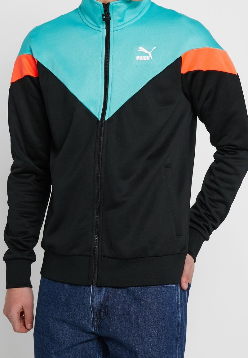 Chaqueta negra con cremallera y detalles en turquesa y naranja. Cuenta con cuello alto, mangas largas y dos bolsillos laterales. Logo de Puma en el pecho.